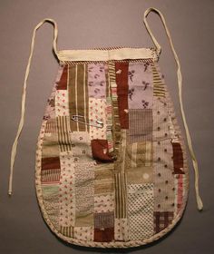 an old patchwork bag is hanging on the wall next to a gray background with white string