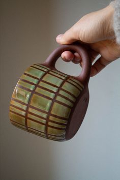 a hand holding a brown and green ceramic teapot in it's right hand