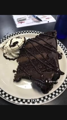 a piece of chocolate cake on a plate with whipped cream and chocolate drizzle