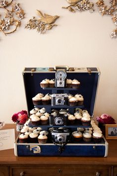 an open suitcase sitting on top of a table filled with cupcakes and muffins