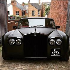 a black sports car parked in front of a brick building with its hood up and lights on