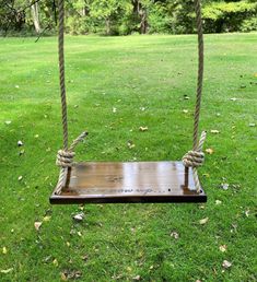 a wooden swing with rope hanging from it's sides in a grassy area next to trees