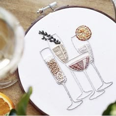 two glasses of wine on a table with oranges and an embroidery pattern in the hoop