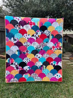 a multicolored quilt on the grass in front of a tree with an umbrella pattern