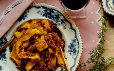 a pasta dish with meat and sauce on a plate next to a cup of coffee