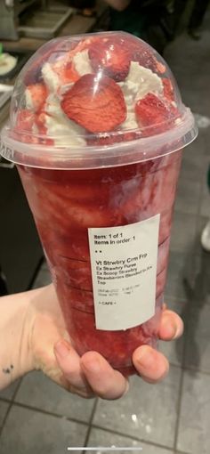 someone holding up a plastic cup with strawberries in it