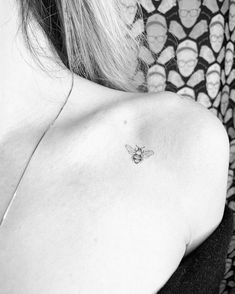 a black and white photo of a woman's shoulder with a bee tattoo on it