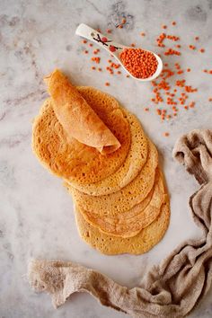 a stack of flatbreads next to a measuring spoon with red lentils on it