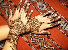 a woman's hand with henna tattoos on her arm and wrist, resting on a colorful rug