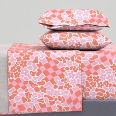 three pillows are stacked on top of each other in front of a bed with pink and white sheets