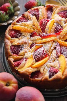 a cake with fruit on top and powdered sugar on the crust, sitting next to some strawberries