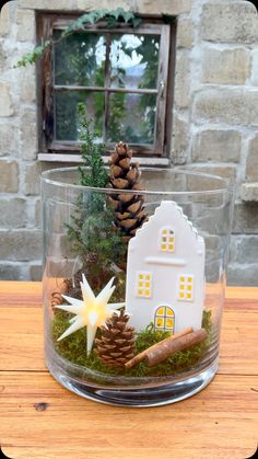 a glass bowl filled with fake pine cones and a small house in the center, sitting on top of a wooden table