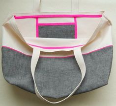 a gray and white bag with pink trimmings on the bottom, sitting on a table