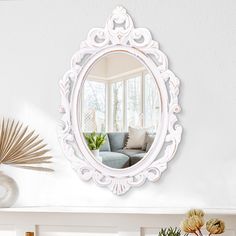 a white mirror sitting on top of a wall next to a vase filled with flowers