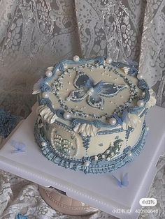 a blue and white decorated cake sitting on top of a table next to a lace curtain