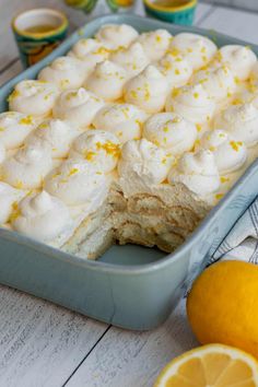 a pan filled with lemon meringue dessert next to sliced oranges and cups