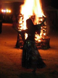 a woman standing in front of a fire with her arms spread out and hands outstretched