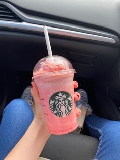 a woman is holding a pink drink in her hand while sitting in the passenger seat of a car