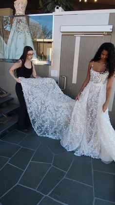 two women standing next to each other in front of a dress