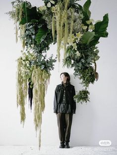 a man standing in front of a bunch of flowers and plants hanging from the ceiling