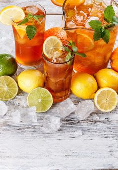 three glasses filled with lemonade, limes and ice on top of a wooden table