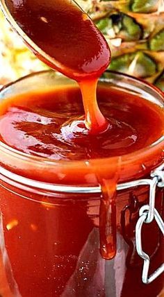 a spoon full of sauce is being poured into a glass jar filled with something else