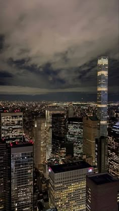 the city skyline is lit up at night, with clouds in the sky above it