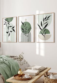 three paintings hang on the wall above a coffee table in a white room with green bedding