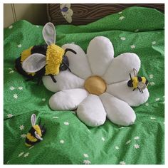 two stuffed bees sitting on top of a bed next to a white and yellow flower