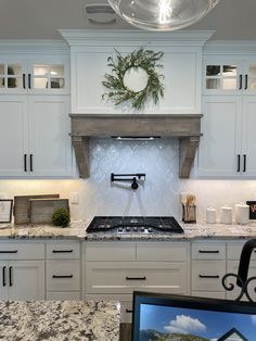 a kitchen with white cabinets and marble counter tops, an oven hood over the stove