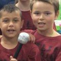 two boys are holding a baseball bat and ball in front of them while others look on