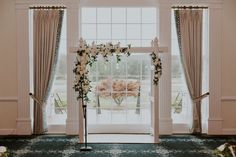 a wedding arch with flowers and greenery in front of a large window at the end of an aisle