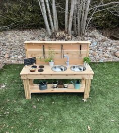 a wooden bench with two sinks and potted plants on it in front of some trees