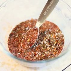 a spoon in a glass bowl filled with seasoning and other things to mix together