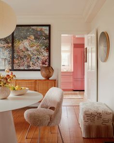 a dining room table with two chairs and a painting on the wall above it, in front of a pink door