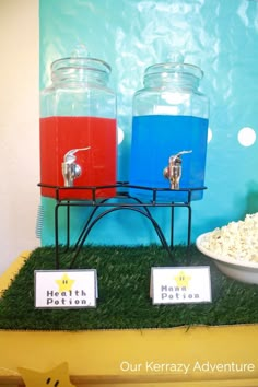 there are two jars with drinks in them on the grass next to a bowl of popcorn