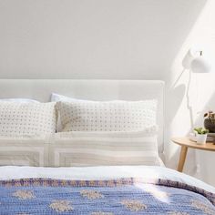 a bed with white sheets and blue bedspread next to a lamp on a table