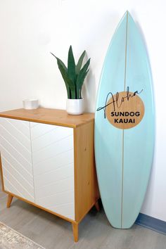 a surfboard leaning against a wall next to a cabinet with a potted plant