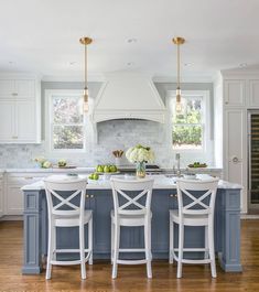 a kitchen with white cabinets and blue island in the center is surrounded by stools