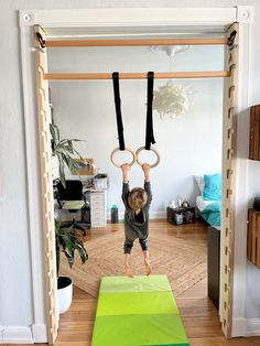 a young child is doing aerial exercises on rings in the living room while holding onto their hands