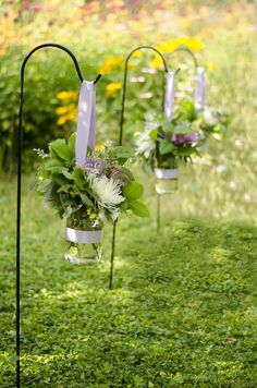 three vases filled with flowers and greenery on top of a grass covered field