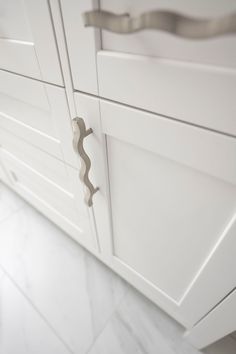 a close up of a cabinet door handle on a white kitchen cupboards with marble flooring