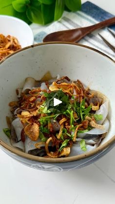 a bowl filled with noodles and vegetables on top of a white table next to chopsticks