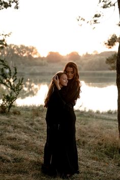 two women standing next to each other in front of a body of water at sunset