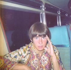 a young man sitting on top of a bus talking on a cell phone while holding his hand up to his ear