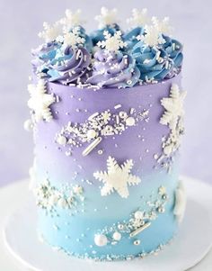 there is a blue and purple cake with white flowers on the top, and snow flakes all over it