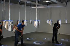 several people standing in an art gallery looking at artwork hanging from the ceiling and talking to each other