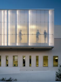 three people are standing in front of a building with glass walls and lights on it