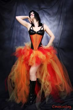 a woman dressed in an orange and black corset with her hands on her hips