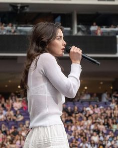 a woman holding a microphone while standing in front of a crowd at a sporting event